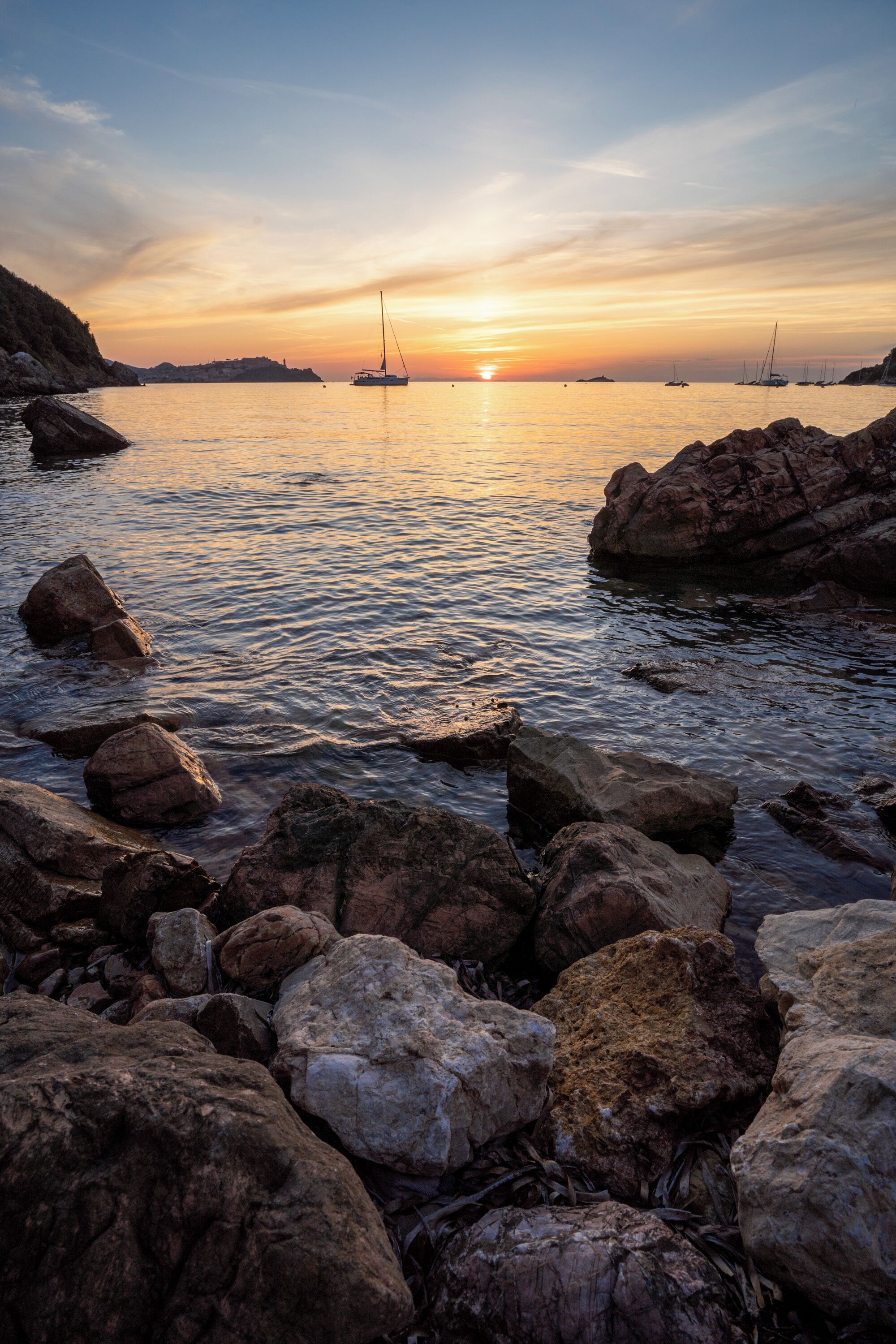 A rocky shoreline with boats at sunset.