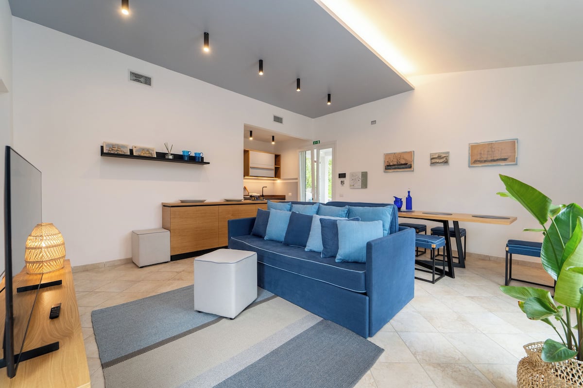 A modern living room with a blue sofa, a wooden coffee table, and a dining area with a wooden table and chairs.