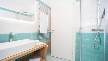 A modern bathroom with a large white sink, a wooden vanity, a glass shower enclosure, and teal and white tiled walls.
