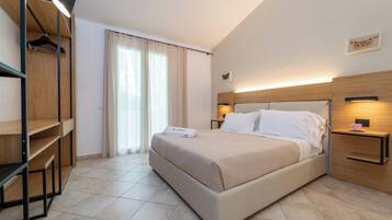 Ein modernes Hotelzimmer mit einem großen Bett, einem Holzschrank, einem Nachttisch mit Lampe und einem Fenster mit Vorhängen.