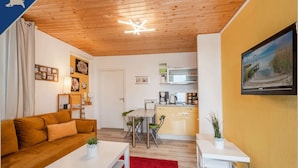 Un espacio habitable compacto con techo de madera, una kitchenette, un sofá, una mesa de comedor y un televisor montado en la pared.