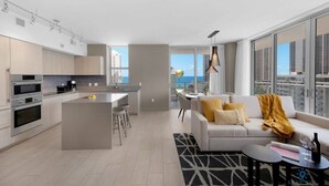 A modern apartment with a kitchen, dining area, and living room. It features a large window with a city view, a sofa with cushions, and a small coffee table. - Beautiful apartment with Amazing Pool, Balcony (Hollywood)