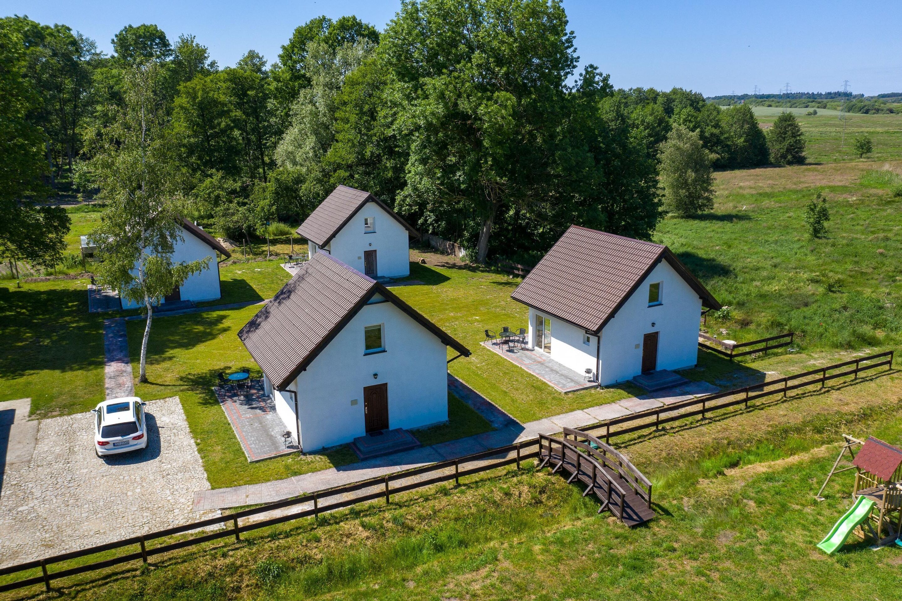 Three white buildings with brown roofs, surrounded by green grass and trees.