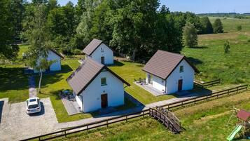 Three white buildings with brown roofs, surrounded by green grass and trees.