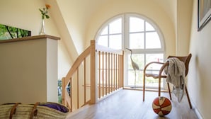 Ein Zimmer mit einer Holztreppe, einem großen Bogenfenster, einem Korbstuhl und einem Basketball auf dem Boden.