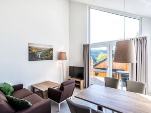 Een moderne woonkamer met een bank, stoelen, een tafel, een televisie en een schilderij.