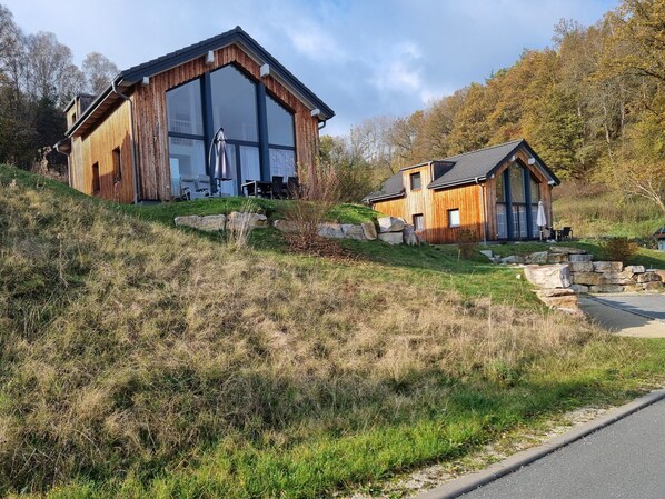 Een modern houten huis met grote ramen en een kiezelpad dat naar de ingang leidt.