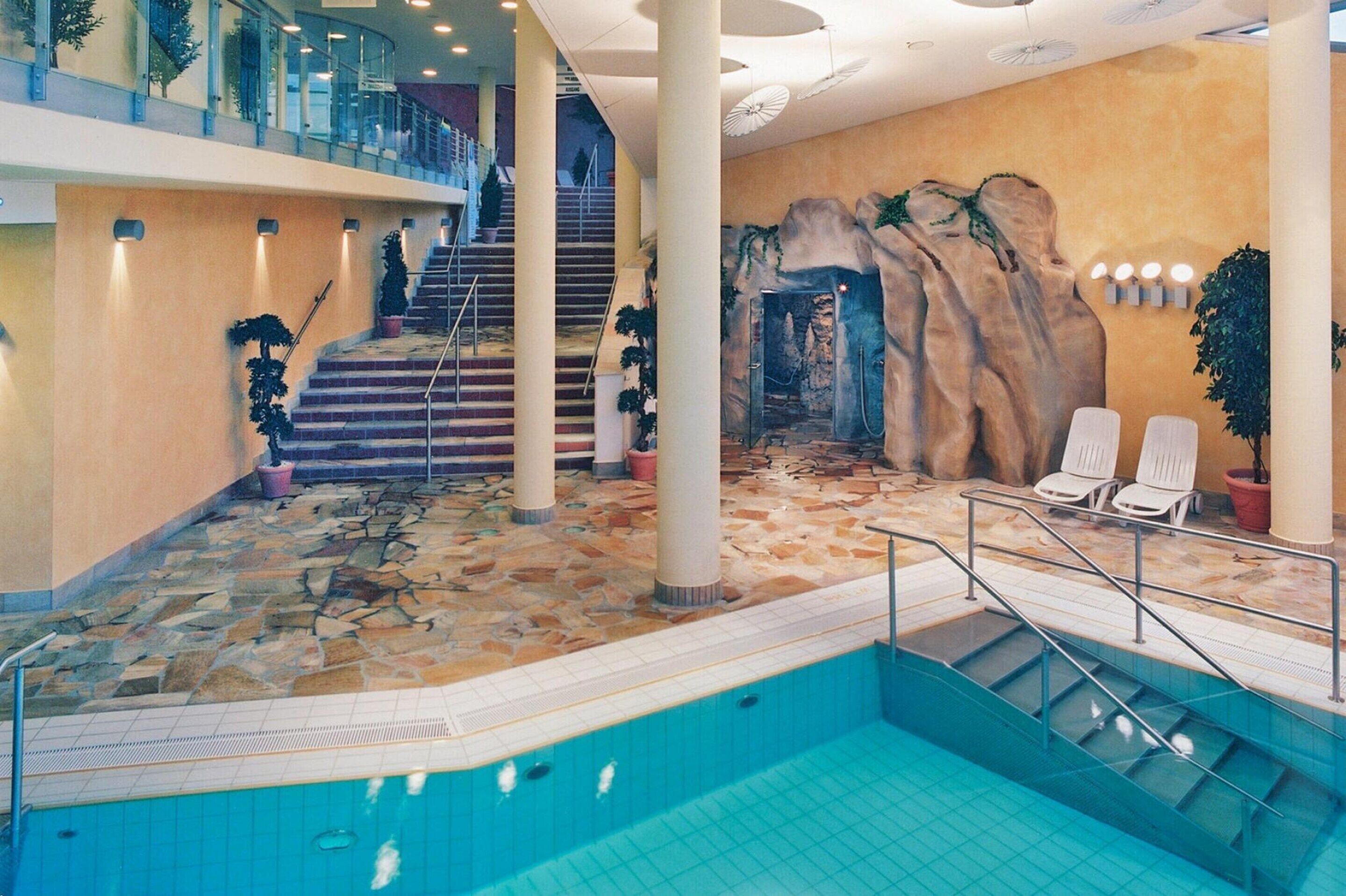 An indoor swimming pool with stone flooring, a staircase, and a rock wall mural.