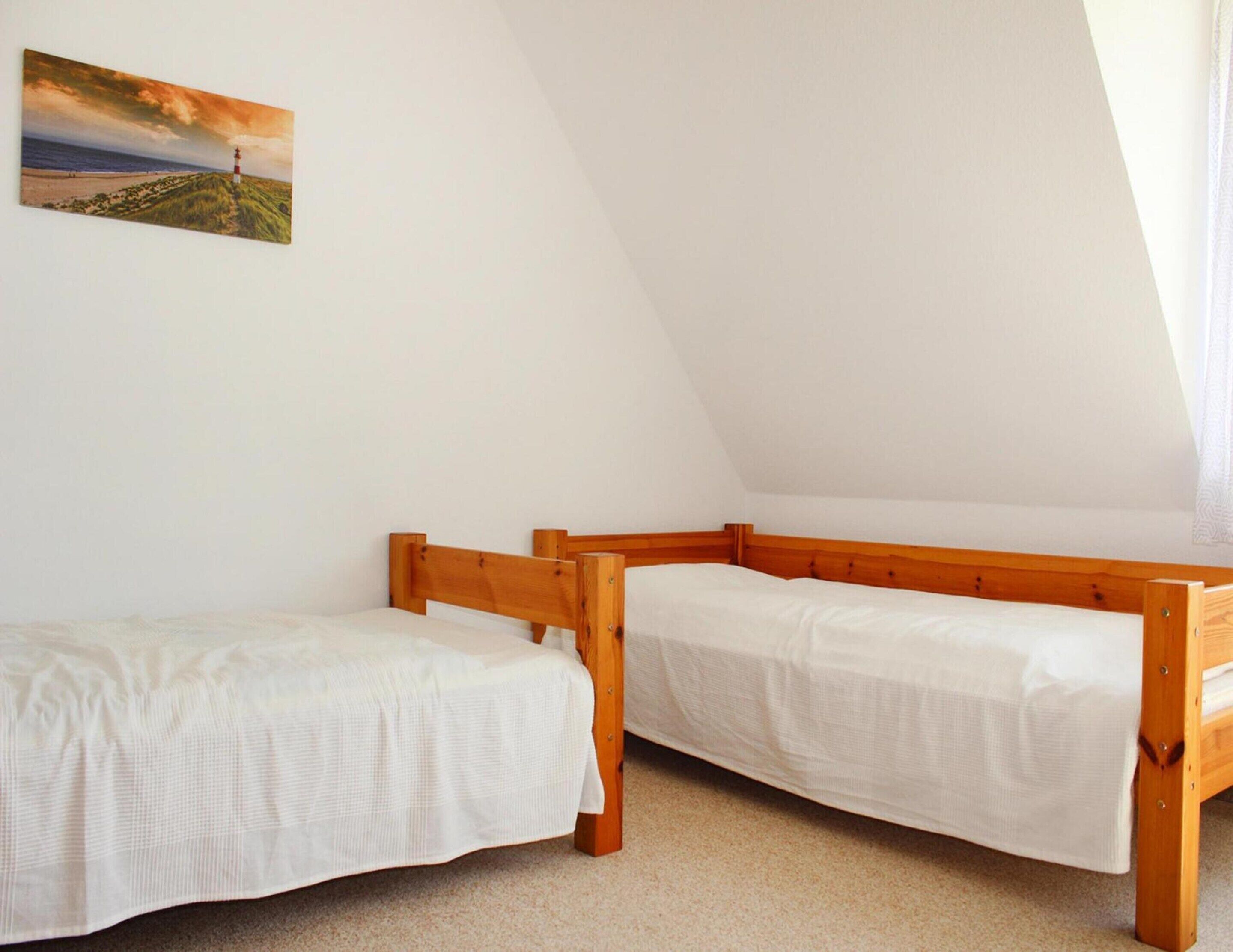 A small, triangular attic bedroom with two wooden bunk beds and a painting of a lighthouse on the wall.