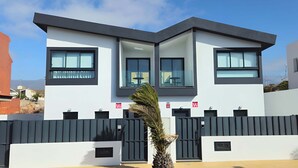 Un edificio moderno de dos pisos con amplios ventanales, una entrada con portón y una palmera en primer plano.
