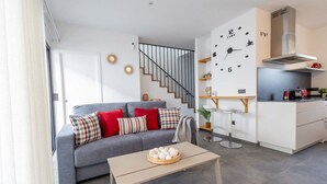 A modern living room with a grey sofa, a coffee table, and a kitchen area with a stove and cabinets.