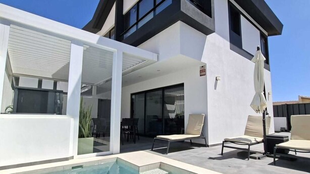 A modern two-story house with a swimming pool, outdoor seating, and a covered patio area.