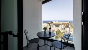 A balcony with a table, two chairs, a bottle of wine, and a view of the sea and buildings.