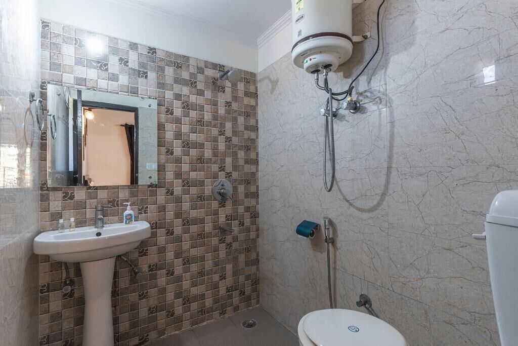 A bathroom with a tiled shower wall, a sink with a mirror, and a toilet.