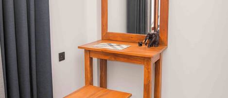 Una habitación con un escritorio y silla de madera, un espejo, un reloj y cortinas grises.