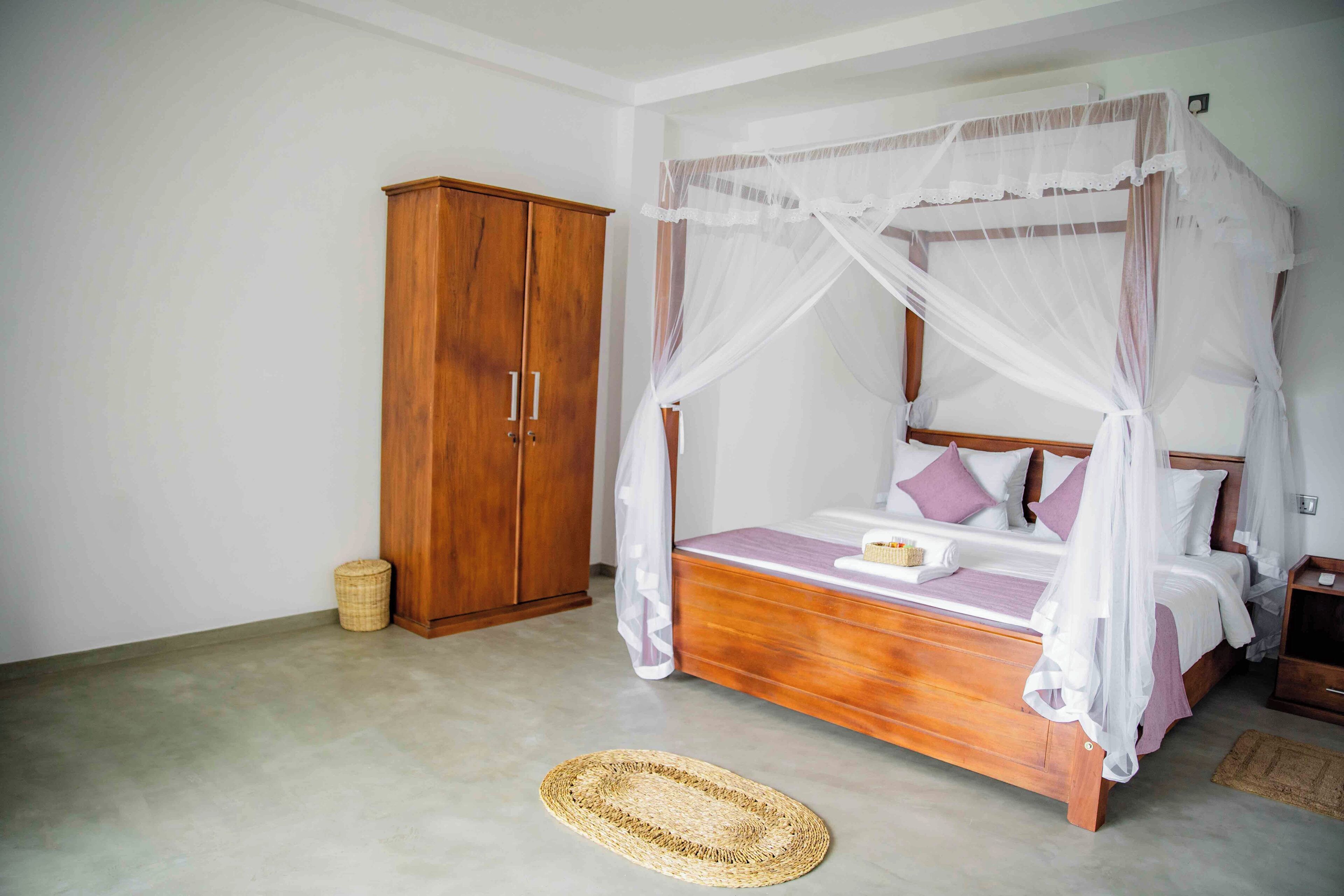 Un dormitorio con una cama de dosel de madera, un armario de madera y un tapete tejido en el suelo.