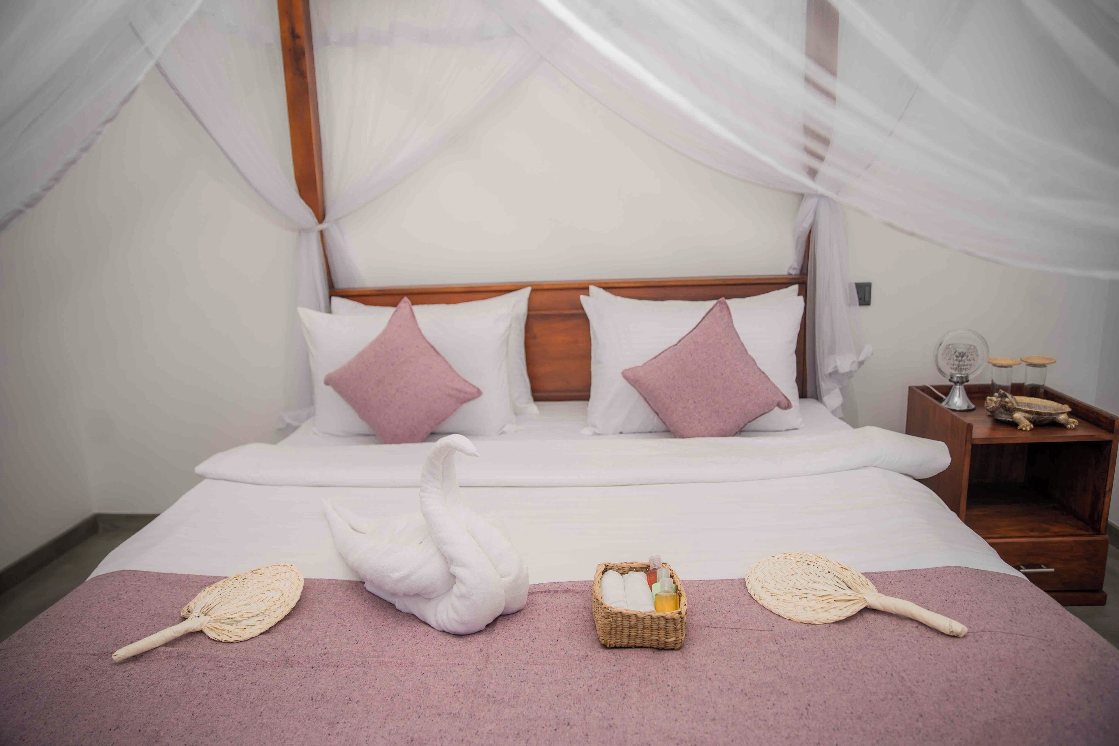 Una cama elegantemente arreglada con dosel, una decoración con forma de cisne y una pequeña cesta con artículos de aseo.