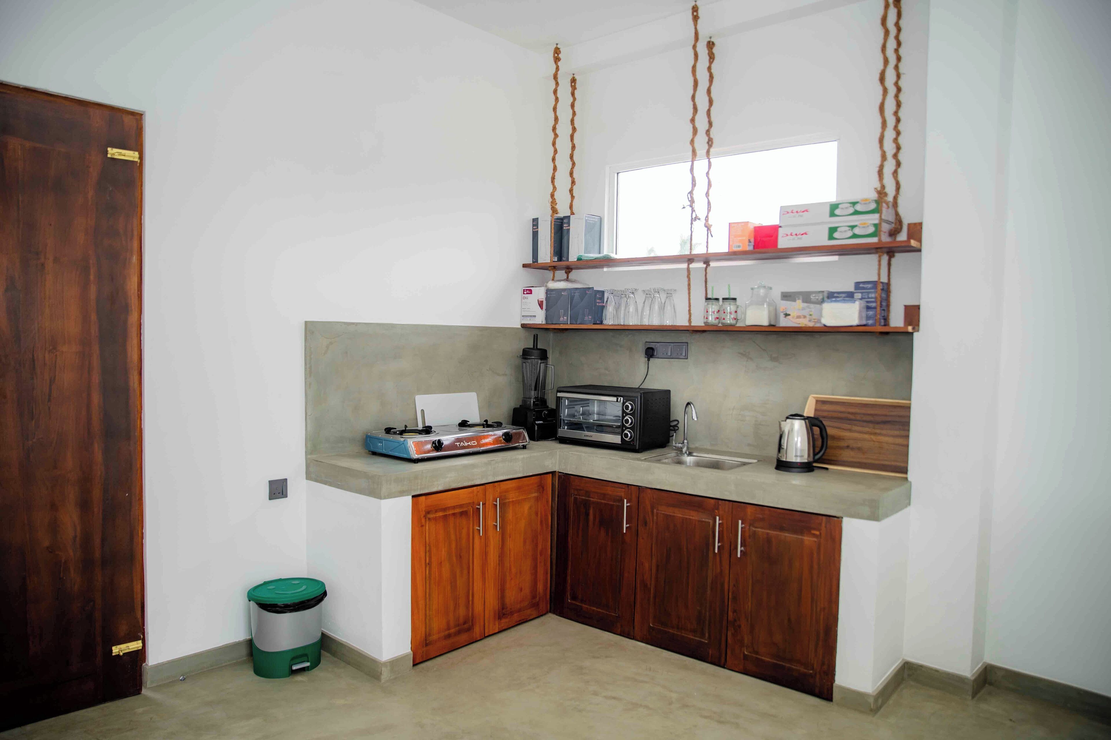 Cocina compacta con armarios de madera, estufa a gas, tostadora y estante colgante con utensilios de cocina.