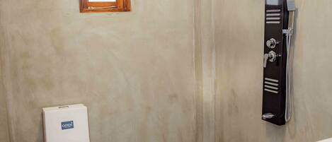 A bathroom with a toilet, a shower, and a small window.