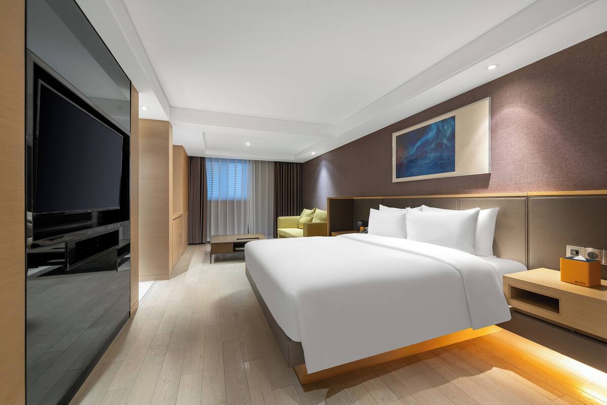 Une chambre d’hôtel moderne dotée d’un grand lit, d  ’un téléviseur à écran plat, d’une table de chevet et d’une œuvre d’art accrochée au mur.