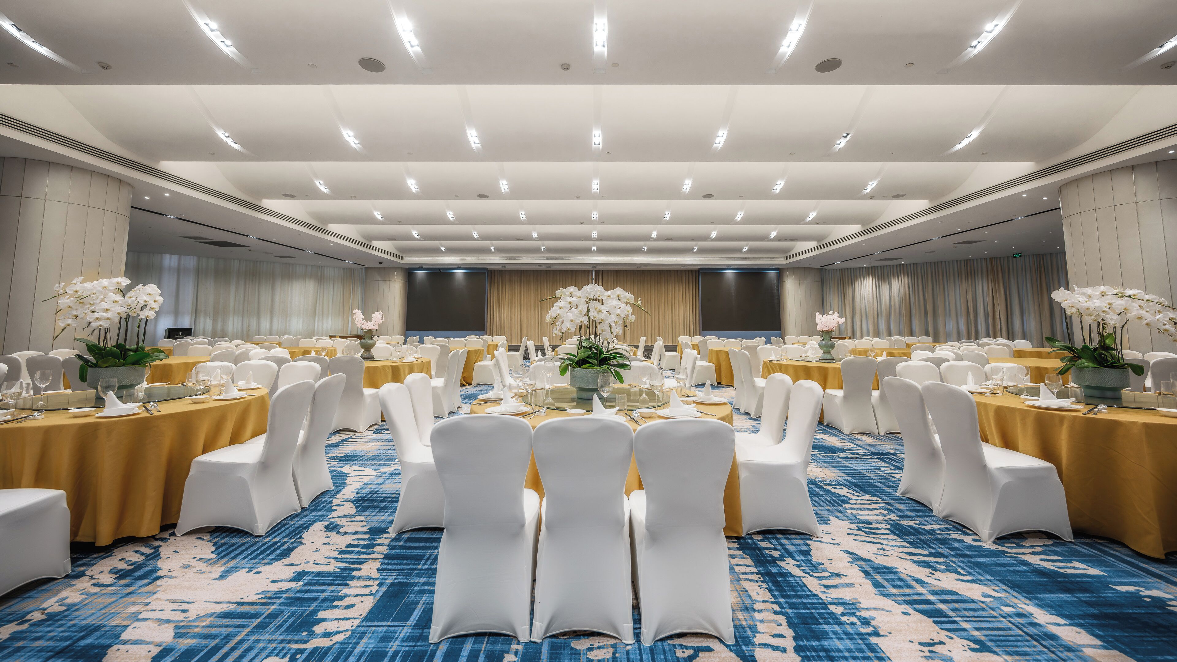 A large banquet hall with round tables, white chairs, and floral centerpieces.
