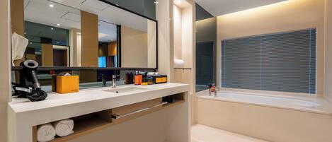 A modern bathroom with a large mirror, dual sinks, a towel rack, and a window with blinds.