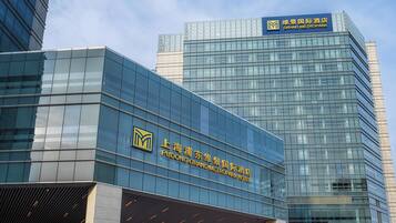 A modern hotel building with a glass facade and signage for Pudong Grand Metropole Hotel.