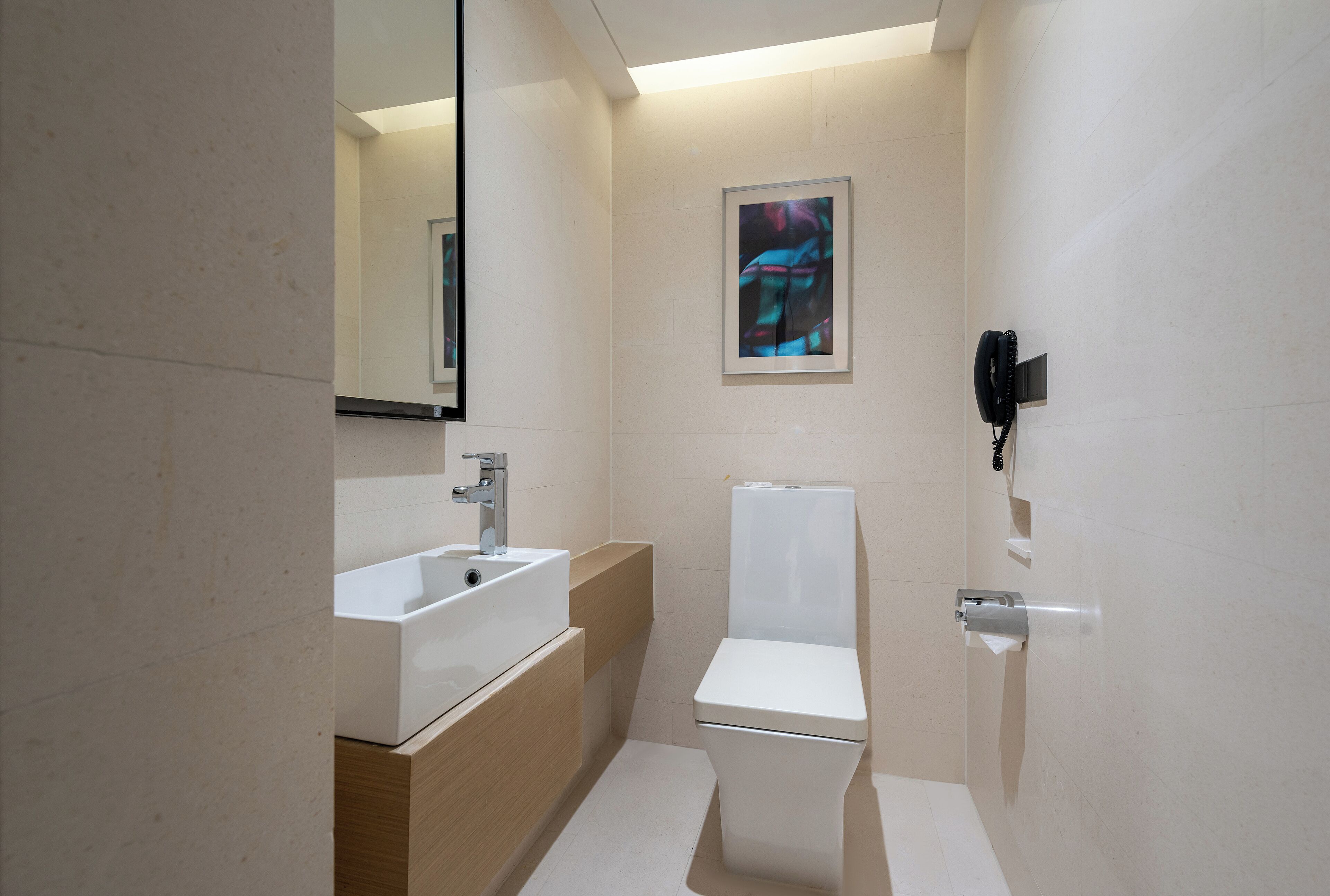 Ein modernes Badezimmer mit einem weißen Waschbecken, einer Toilette und einer Dusche. An der Wand hängt ein gerahmtes Kunstwerk und ein Telefon ist an der Wand montiert.
