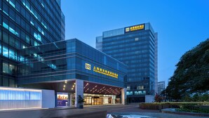 Ein modernes Hotel mit Glasfassade, Beschilderung mit 'Pudong Grand Metropole Hotel' und einem gut beleuchteten Eingangsbereich.