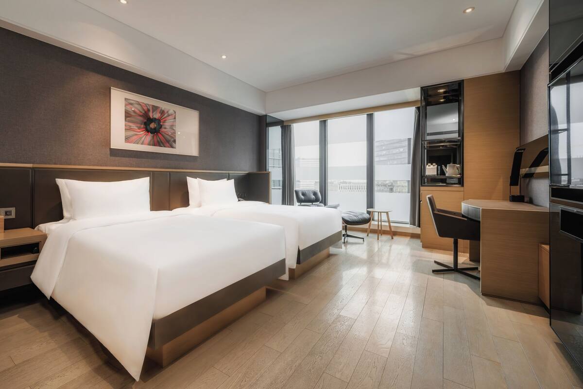 Une chambre d’hôtel moderne avec deux lits, un bureau et une grande fenêtre donnant sur la ville.