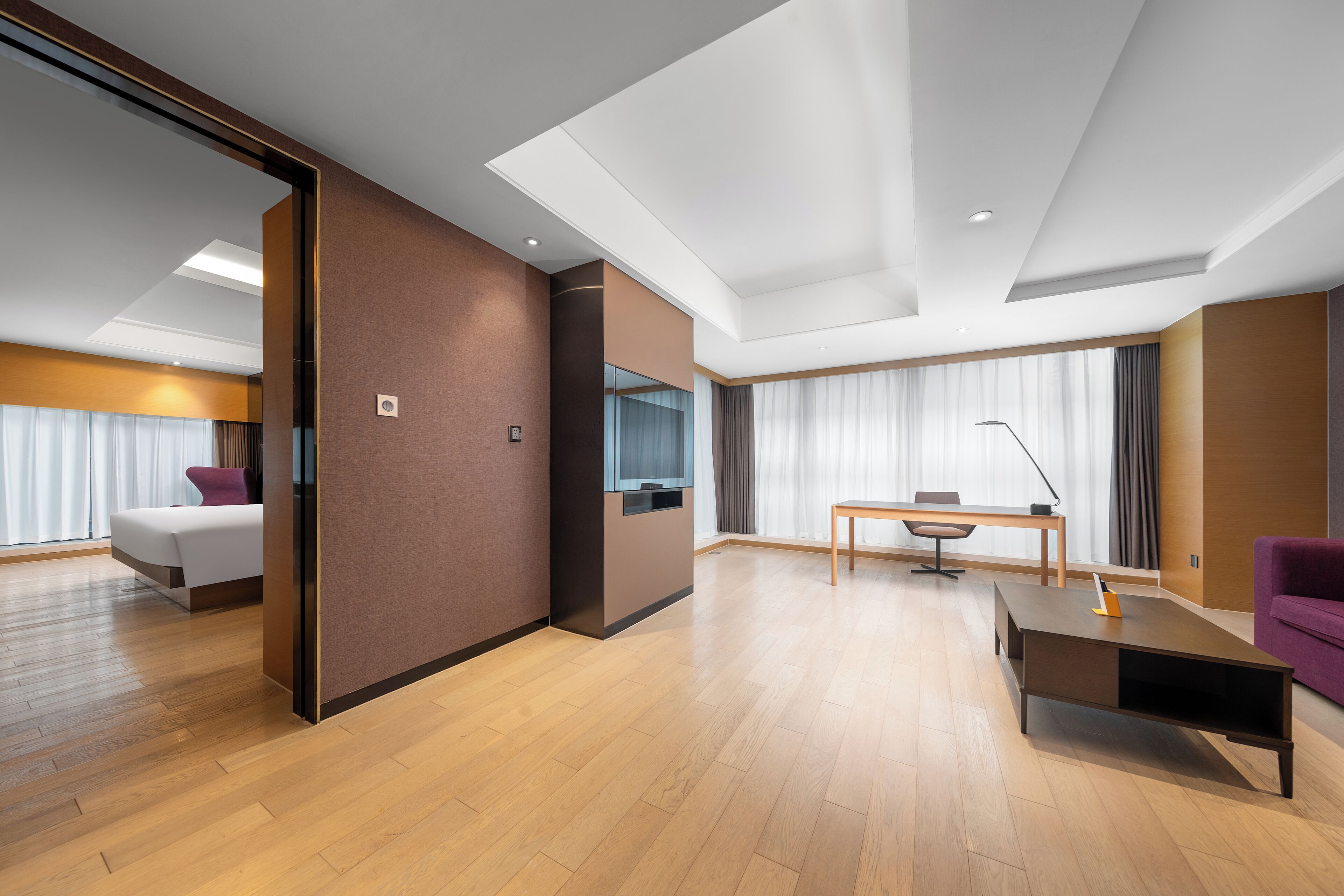 Una habitación de hotel moderna con suelo de madera, una cama, un escritorio y un sofá morado.