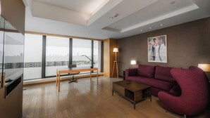 Ein modernes Wohnzimmer mit großem Fenster, einer Couch, einem Couchtisch und einem Schreibtisch.