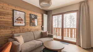 Ein gemütliches Wohnzimmer mit Holzwand, einer Couch, einem runden Tisch und einem Balkon mit Blick auf Bäume.