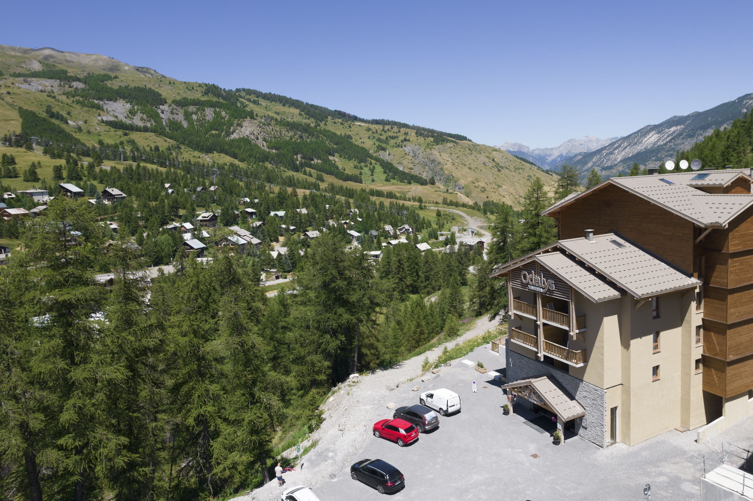En fjeldhytte med parkeringsplads, omgivet af skov og bjerge.