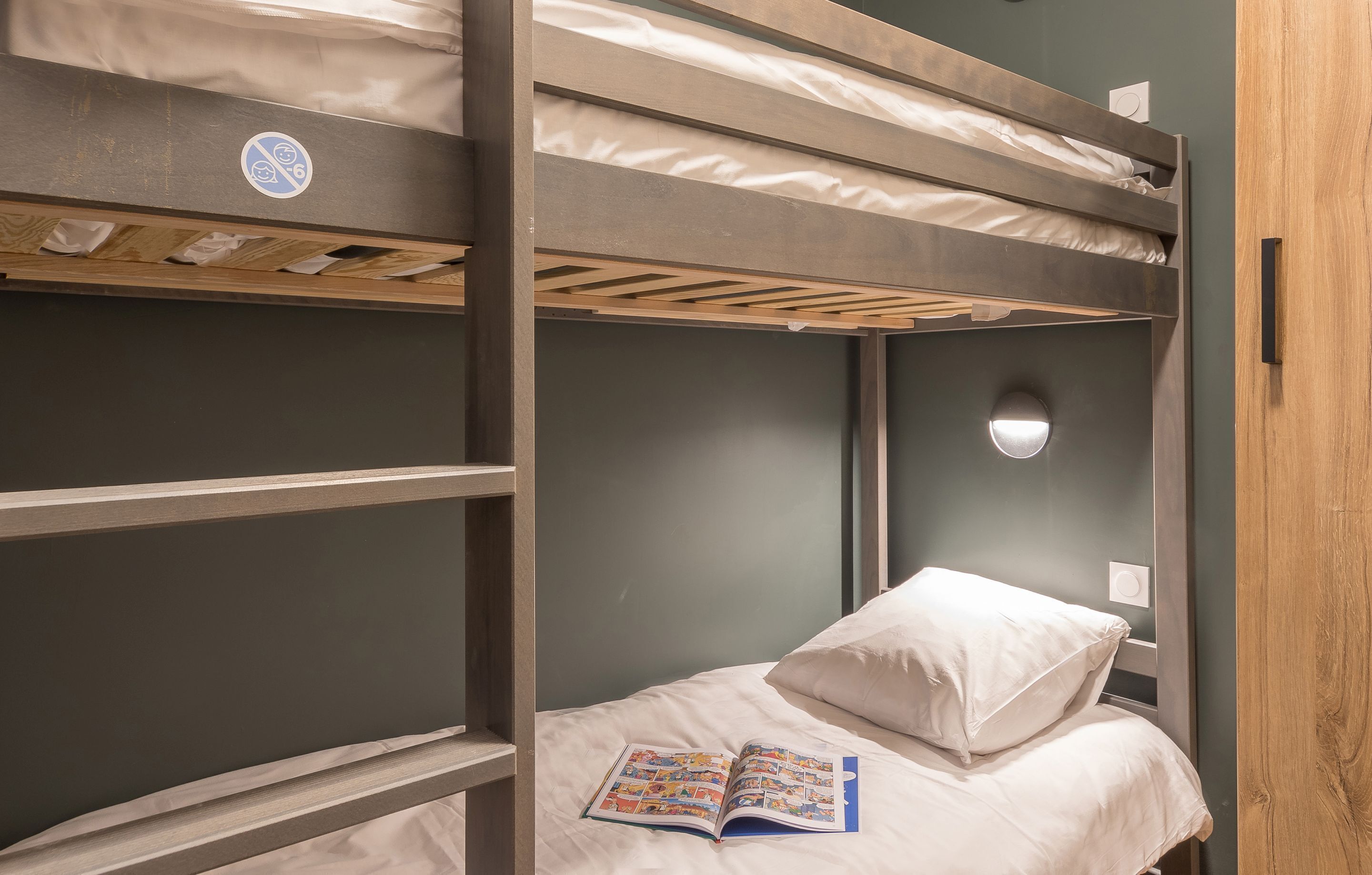 A bunk bed room with a single bed, a night light, and a book on the bed.