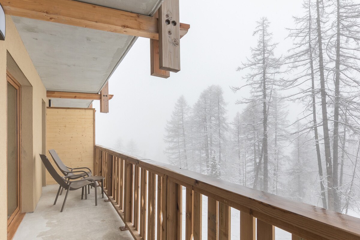 A wooden balcony with a view of snow-covered trees.