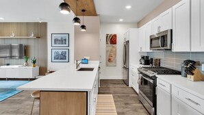 Une cuisine moderne avec des meubles blancs, un îlot central, des appareils en acier inoxydable et des luminaires suspendus.