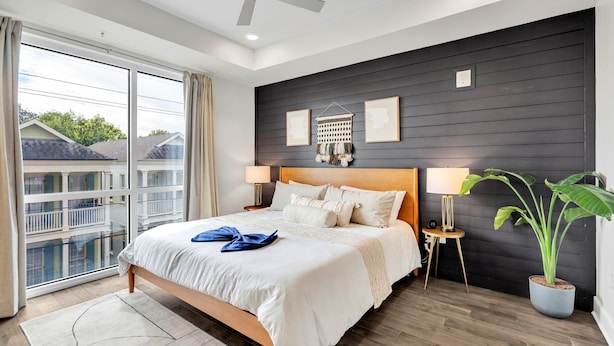 Une chambre moderne avec un grand lit, un ventilateur de plafond, une vue sur un balcon et une plante en pot.