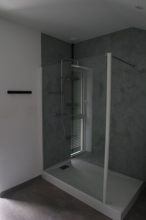 Shower features a handheld and fixed showerhead, mounted on a wall-mounted control panel.
