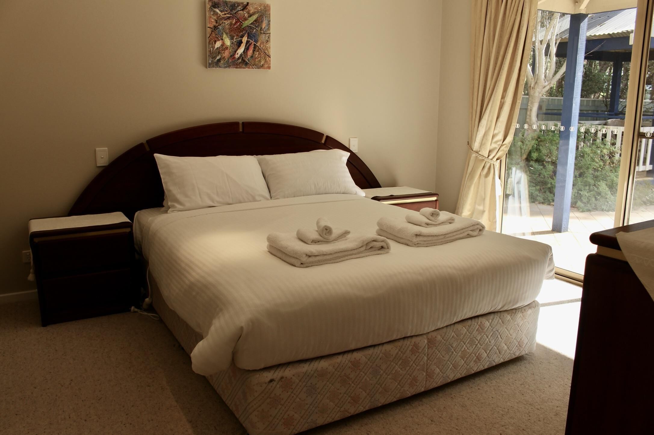 A neatly made bed with two folded towels, a bedside table, and a nightstand.