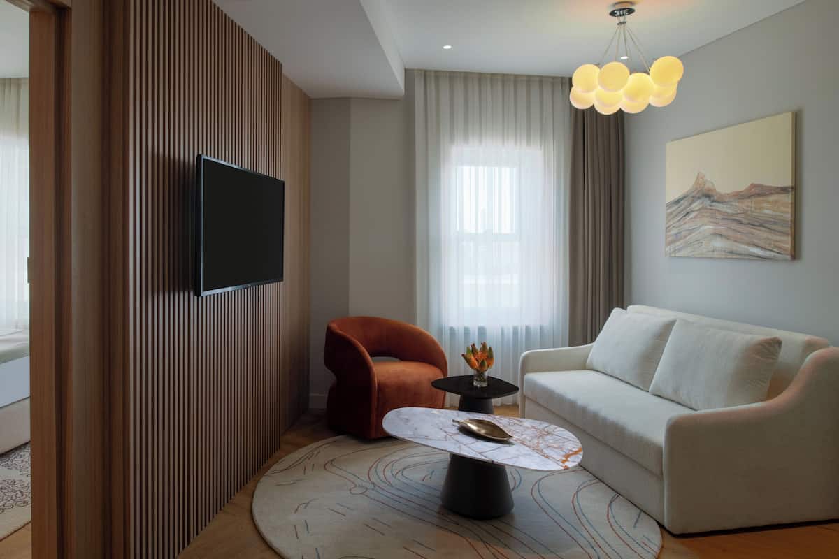 Ein modernes Wohnzimmer mit einem an der Wand befestigten Flachbildfernseher, einem weißen Sofa, einem roten Sessel und einem Couchtisch mit Marmorplatte.