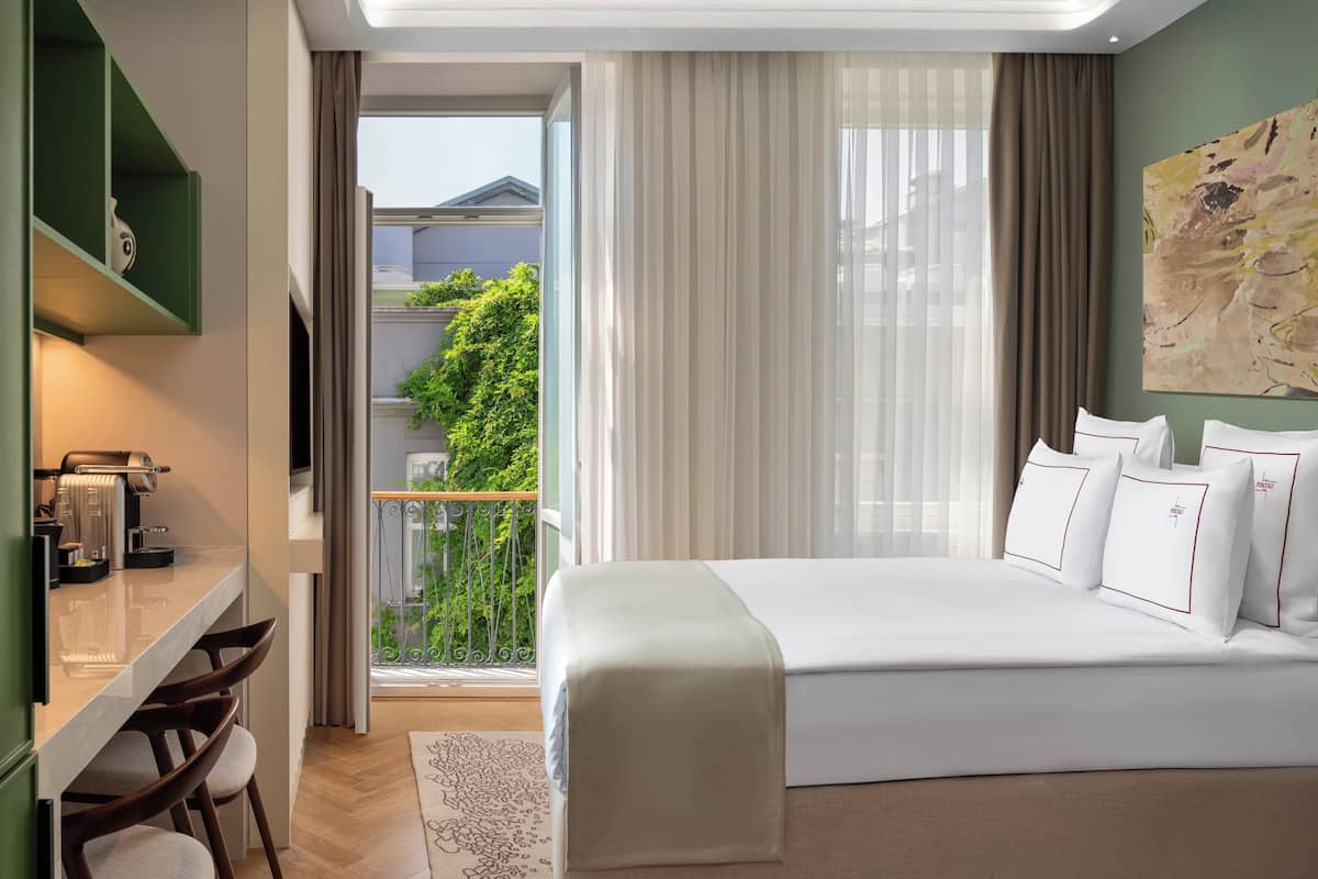 Ein modernes Hotelzimmer mit einem großen Bett, einem Schreibtisch mit Kaffeemaschine und einem Balkon mit Blick auf Grünflächen.