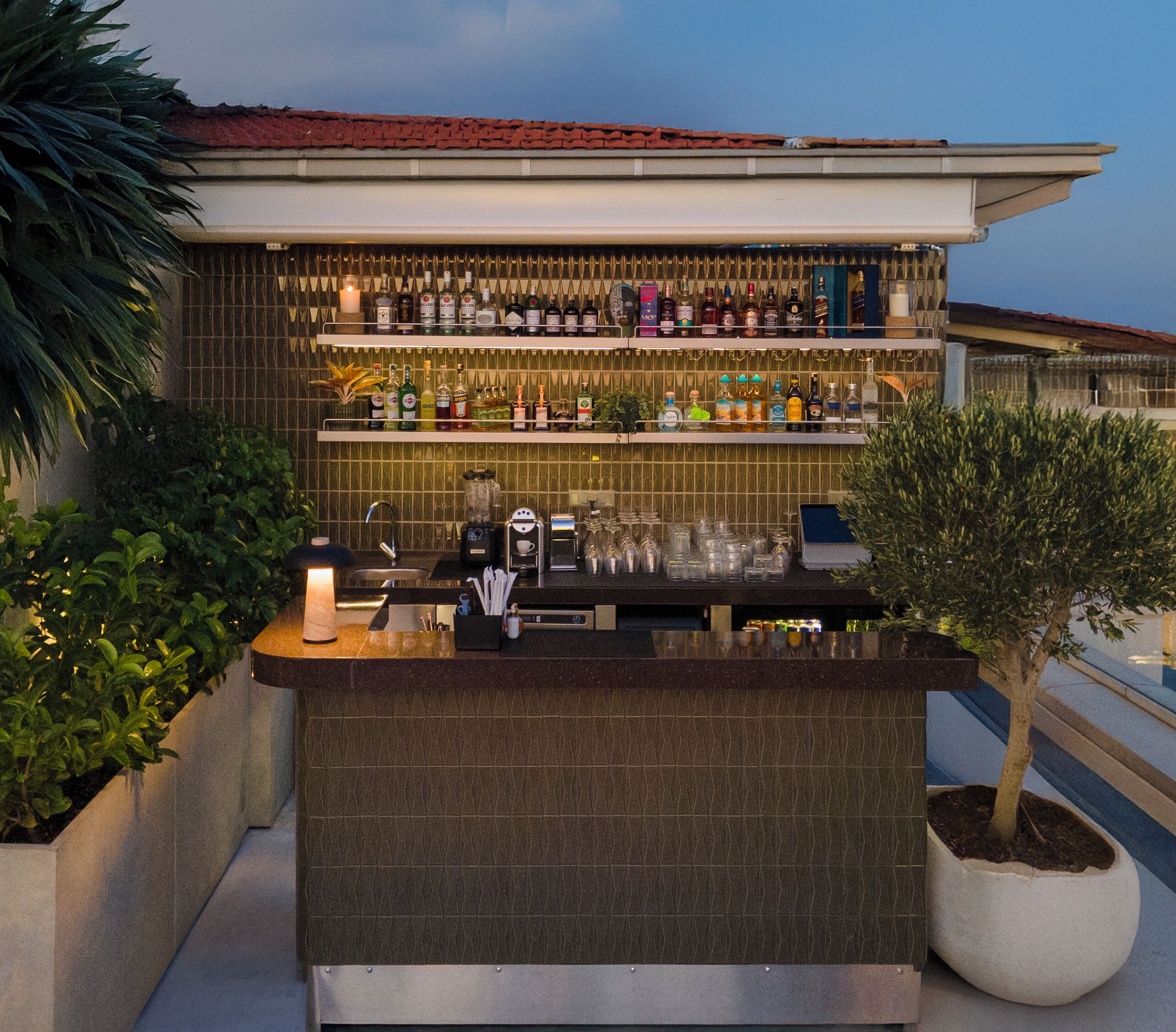 A rooftop bar with a tiled counter, various bottles, glasses, and a coffee machine.