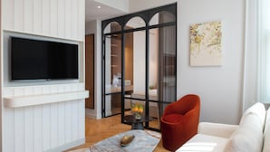 A modern living room with a flat-screen TV mounted on a white wall, a red armchair, a white sofa, and a marble coffee table. - Casa Foscolo Hotel, Istanbul, a Member of Design Hotels (Istanbul)