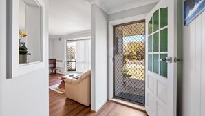 Un couloir avec une porte-fenêtre coulissante donnant sur un balcon, un canapé beige et une plante en pot.
