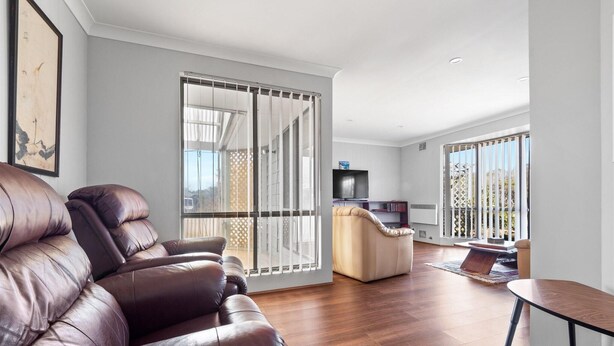Un salon moderne avec un canapé en cuir, un canapé beige et une petite table. On y trouve un téléviseur posé sur un meuble et un balcon avec vue.