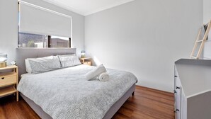 Une chambre à coucher moderne avec un grand lit, des tables de chevet, un miroir et une échelle en bois.