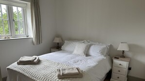 A neatly made bed with white linens and two pillows, a bedside table with a lamp, and a window with curtains. - Lodge/ Kingbed/ Privg/ Petsok/ Freep/ Wifi (Dorchester)