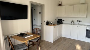 A compact kitchen with white cabinets, a wooden dining table with two chairs, and a flat-screen TV mounted on the wall. - Lodge/ Kingbed/ Privg/ Petsok/ Freep/ Wifi (Dorchester)