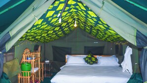 A tented accommodation with a bed, wooden furniture, and a hanging light fixture. - Pacha Waterfront Nithi (Chuka)